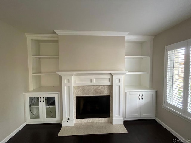 unfurnished living room with a tiled fireplace, crown molding, built in shelves, and dark hardwood / wood-style floors