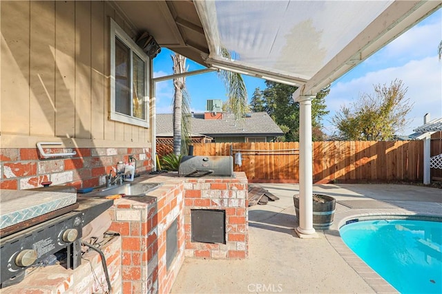 view of patio featuring a fenced in pool, area for grilling, sink, and an outdoor kitchen