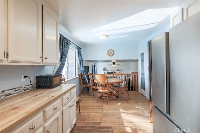 kitchen featuring ceiling fan, wood counters, stainless steel fridge, white cabinets, and light wood-type flooring