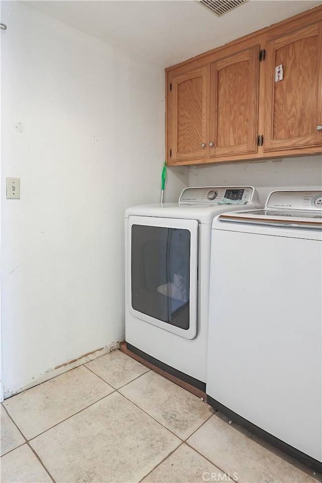 laundry room featuring washing machine and clothes dryer, light tile patterned floors, and cabinets