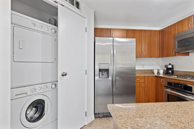 kitchen featuring stacked washer and dryer, light tile patterned floors, and appliances with stainless steel finishes