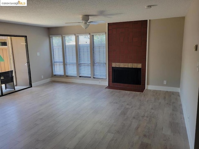 unfurnished living room with a large fireplace, ceiling fan, light hardwood / wood-style floors, and a textured ceiling