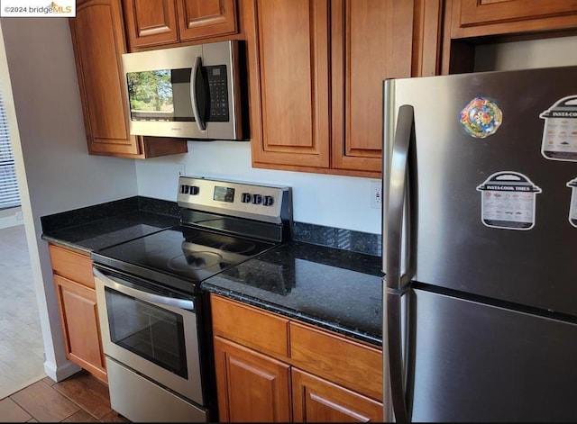 kitchen with wood-type flooring, appliances with stainless steel finishes, and dark stone counters