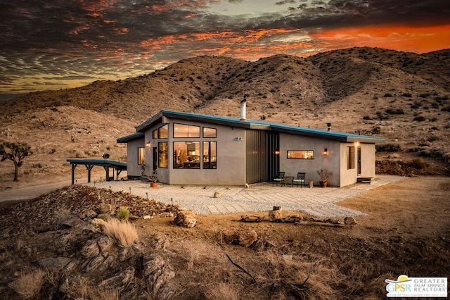 back house at dusk with a mountain view and a patio