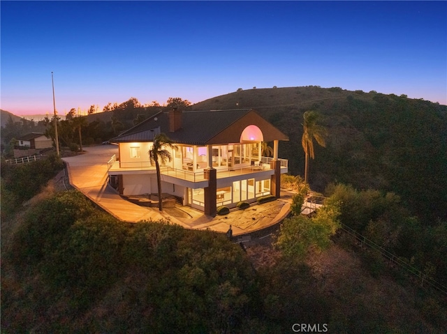 back house at dusk featuring a balcony and a patio