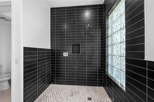 bathroom with tiled shower, toilet, and tile walls