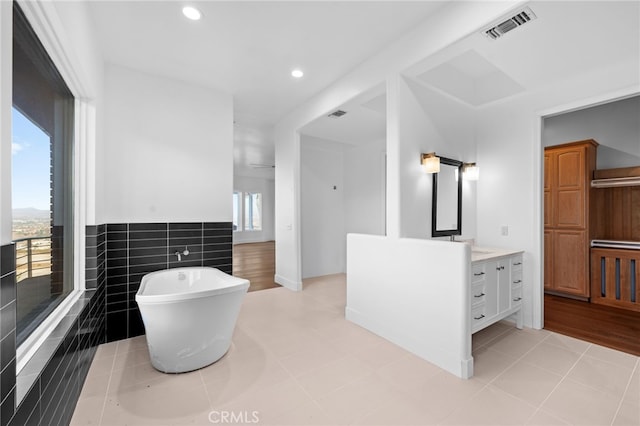 bathroom with a wealth of natural light, a bathtub, vanity, and tile walls