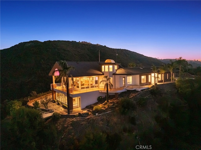 back house at dusk featuring a mountain view and a balcony