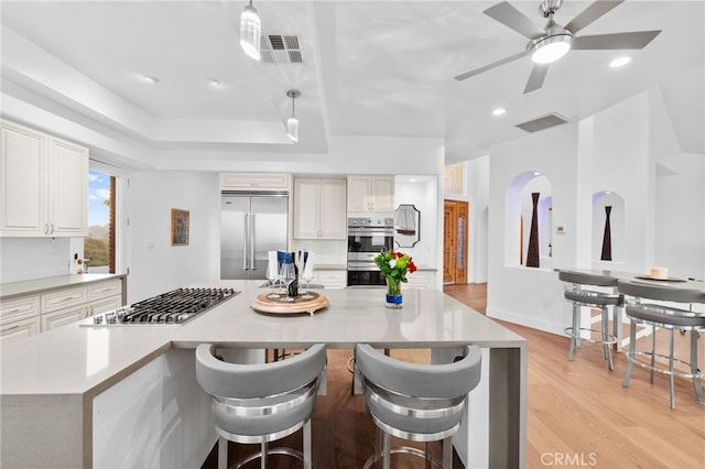 kitchen with a spacious island, hanging light fixtures, light hardwood / wood-style flooring, appliances with stainless steel finishes, and a breakfast bar area