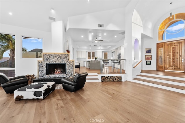 living room with ceiling fan, a fireplace, high vaulted ceiling, and light hardwood / wood-style flooring