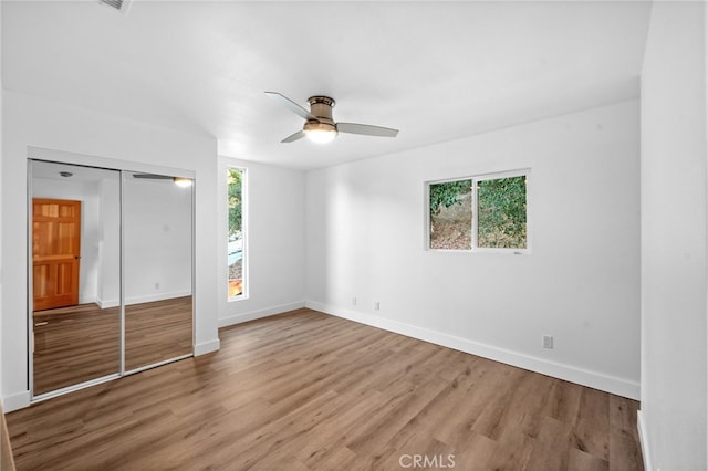 unfurnished bedroom featuring hardwood / wood-style flooring, ceiling fan, a closet, and multiple windows