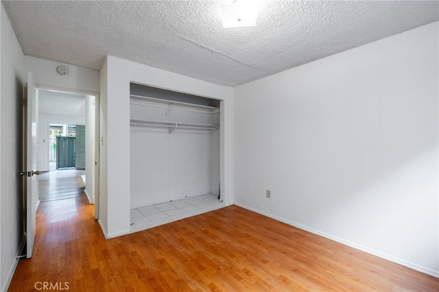 unfurnished bedroom with a textured ceiling, a closet, and light hardwood / wood-style floors