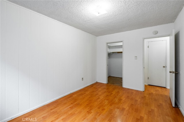 unfurnished bedroom with a closet, a spacious closet, a textured ceiling, and light hardwood / wood-style floors