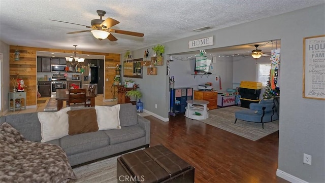 living room with ceiling fan with notable chandelier, hardwood / wood-style floors, a textured ceiling, and wood walls