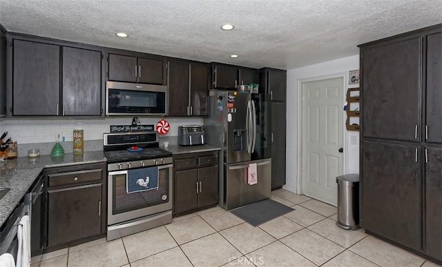 kitchen featuring dark brown cabinetry, stainless steel appliances, dark stone countertops, decorative backsplash, and light tile patterned floors