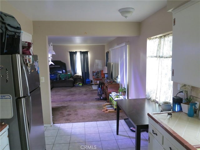 kitchen featuring white cabinets, stainless steel fridge, light colored carpet, and tile countertops