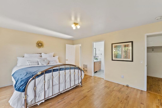 bedroom with ensuite bathroom, a walk in closet, a closet, and light hardwood / wood-style floors