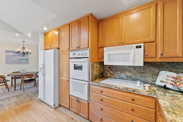 kitchen featuring tasteful backsplash, an inviting chandelier, white appliances, light wood-type flooring, and light stone countertops