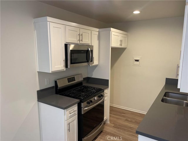 kitchen with wood-type flooring, stainless steel appliances, white cabinetry, and sink