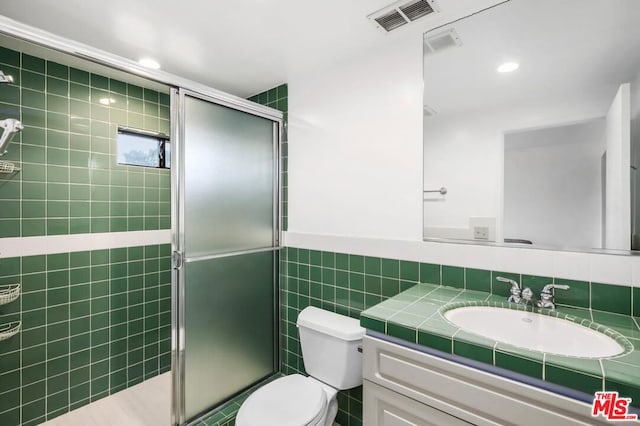 bathroom featuring a shower with door, vanity, tile walls, and toilet