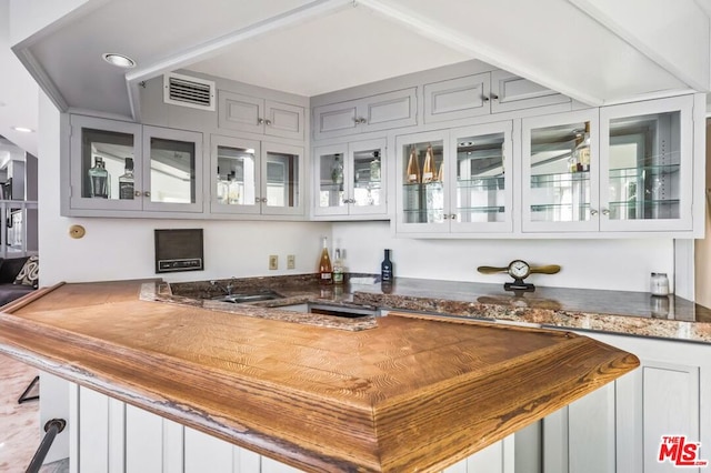 bar featuring sink, gray cabinets, and dark stone countertops