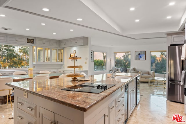 kitchen with sink, gray cabinets, light stone countertops, a large island, and stainless steel refrigerator