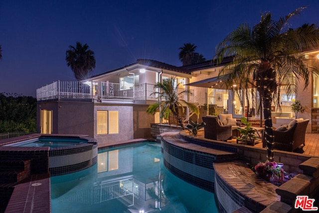 pool at night featuring an in ground hot tub, an outdoor hangout area, and a patio area