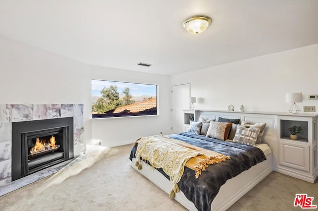 bedroom with a high end fireplace and light colored carpet