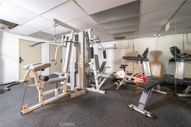 workout room with a wall mounted AC and a paneled ceiling