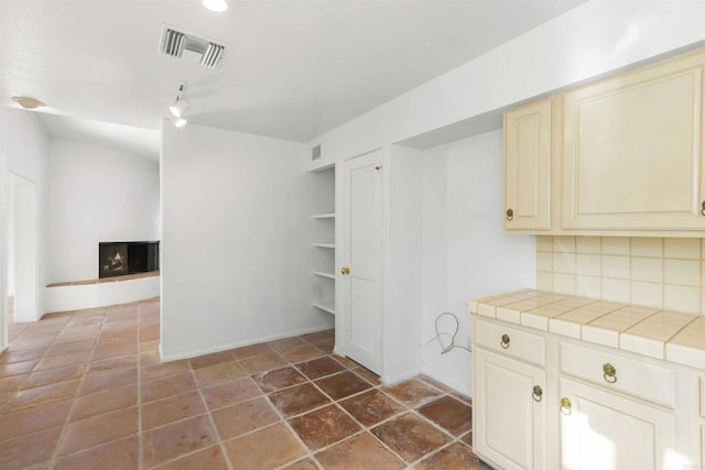 kitchen with decorative backsplash, tile counters, and cream cabinetry