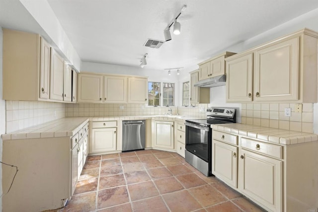 kitchen with tasteful backsplash, tile countertops, track lighting, and appliances with stainless steel finishes