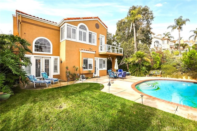 rear view of property featuring a balcony, a patio area, and a lawn