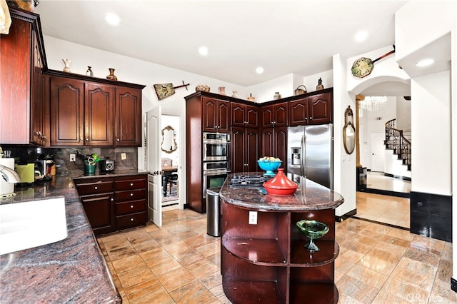 kitchen featuring appliances with stainless steel finishes, dark stone countertops, backsplash, dark brown cabinetry, and a kitchen island