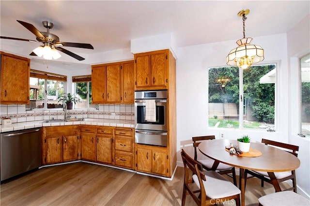 kitchen featuring stainless steel dishwasher, decorative light fixtures, wood-type flooring, and tasteful backsplash