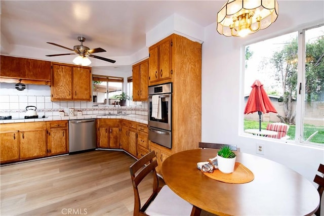 kitchen with appliances with stainless steel finishes, backsplash, ceiling fan with notable chandelier, sink, and light hardwood / wood-style floors