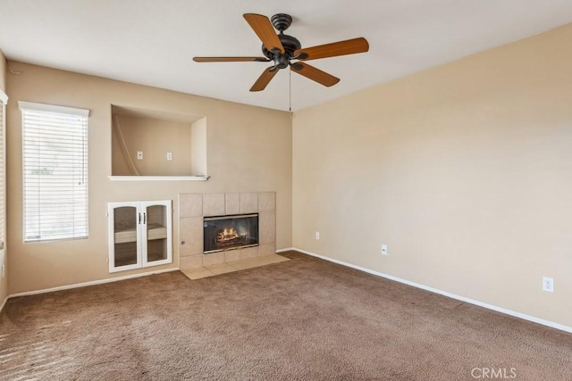 unfurnished living room with a tiled fireplace, carpet floors, and ceiling fan