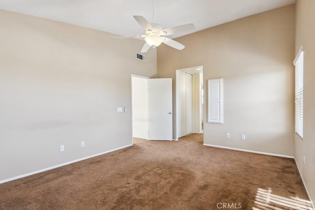 unfurnished room with ceiling fan, a wealth of natural light, a high ceiling, and carpet