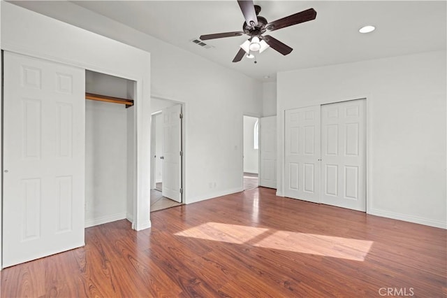 unfurnished bedroom featuring lofted ceiling, hardwood / wood-style flooring, two closets, and ceiling fan