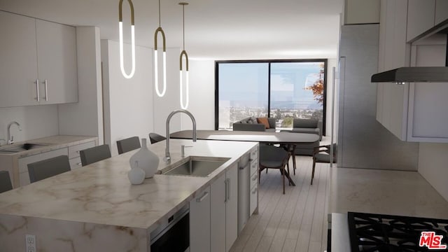 kitchen featuring hanging light fixtures, sink, an island with sink, and white cabinets