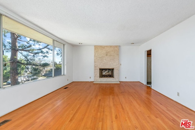 unfurnished living room with a large fireplace, light hardwood / wood-style flooring, and a textured ceiling