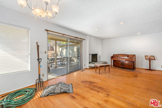 living area featuring a brick fireplace, hardwood / wood-style floors, a textured ceiling, and a chandelier