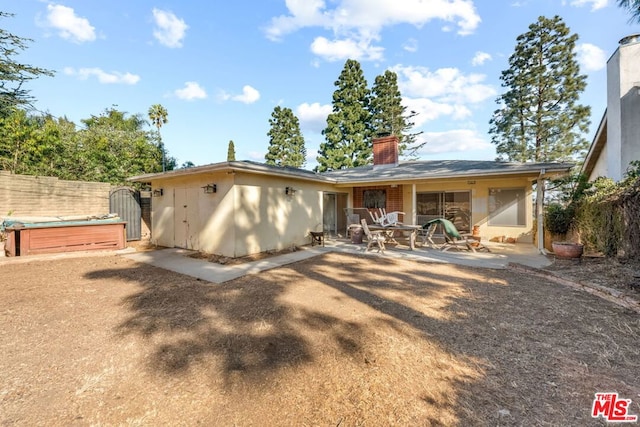 rear view of property with a hot tub and a patio area