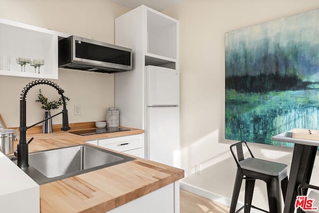 kitchen featuring wood counters, light wood-type flooring, sink, white fridge, and white cabinetry