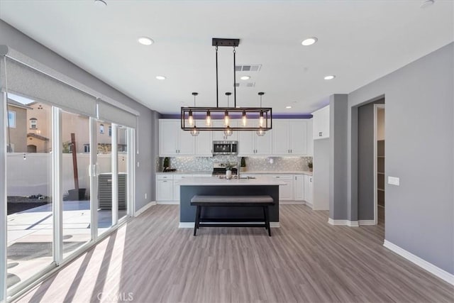 kitchen featuring white cabinetry, backsplash, an island with sink, pendant lighting, and light hardwood / wood-style floors