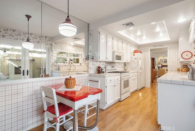 kitchen with white appliances, a raised ceiling, tile countertops, light wood-style floors, and white cabinetry