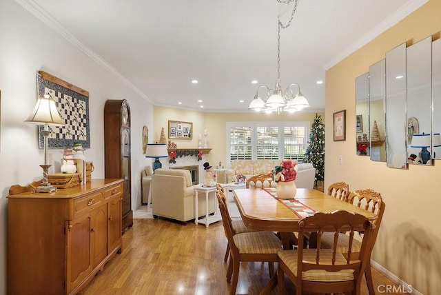 dining space featuring light wood-style flooring, recessed lighting, crown molding, a glass covered fireplace, and an inviting chandelier