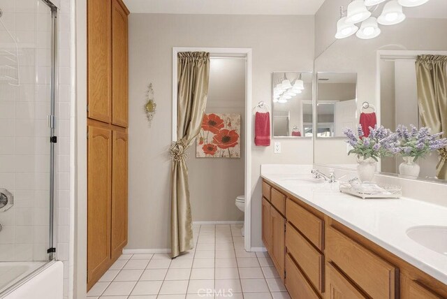 full bath featuring double vanity, toilet, a sink, tile patterned flooring, and baseboards