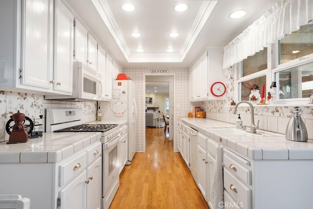 kitchen featuring white appliances, white cabinetry, a raised ceiling, and a sink