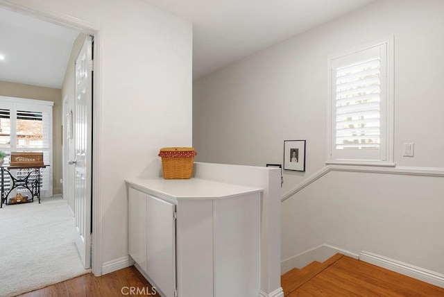 corridor featuring baseboards, wood finished floors, and an upstairs landing