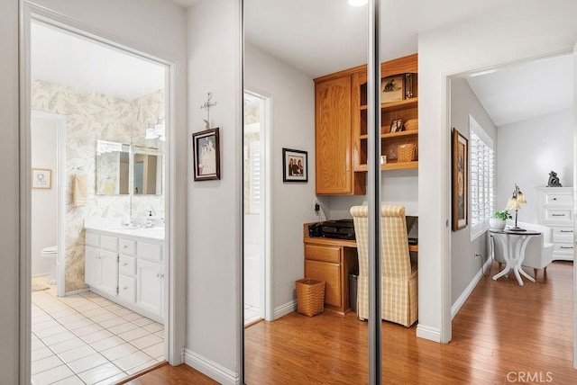 corridor featuring a sink, light wood-style flooring, and baseboards